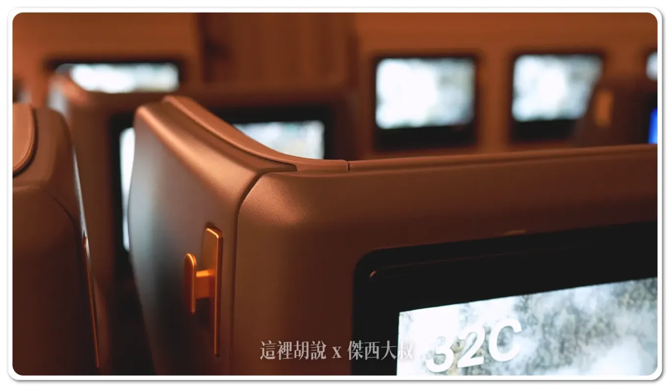 The coat hook is located on the side panel of the seat in front.