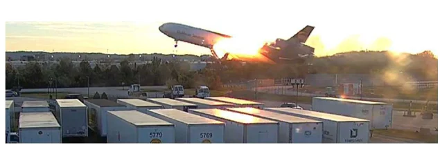 [圖 2：隨著飛機越過防爆牆，左側掛架與機翼連接處區域持續起火。]