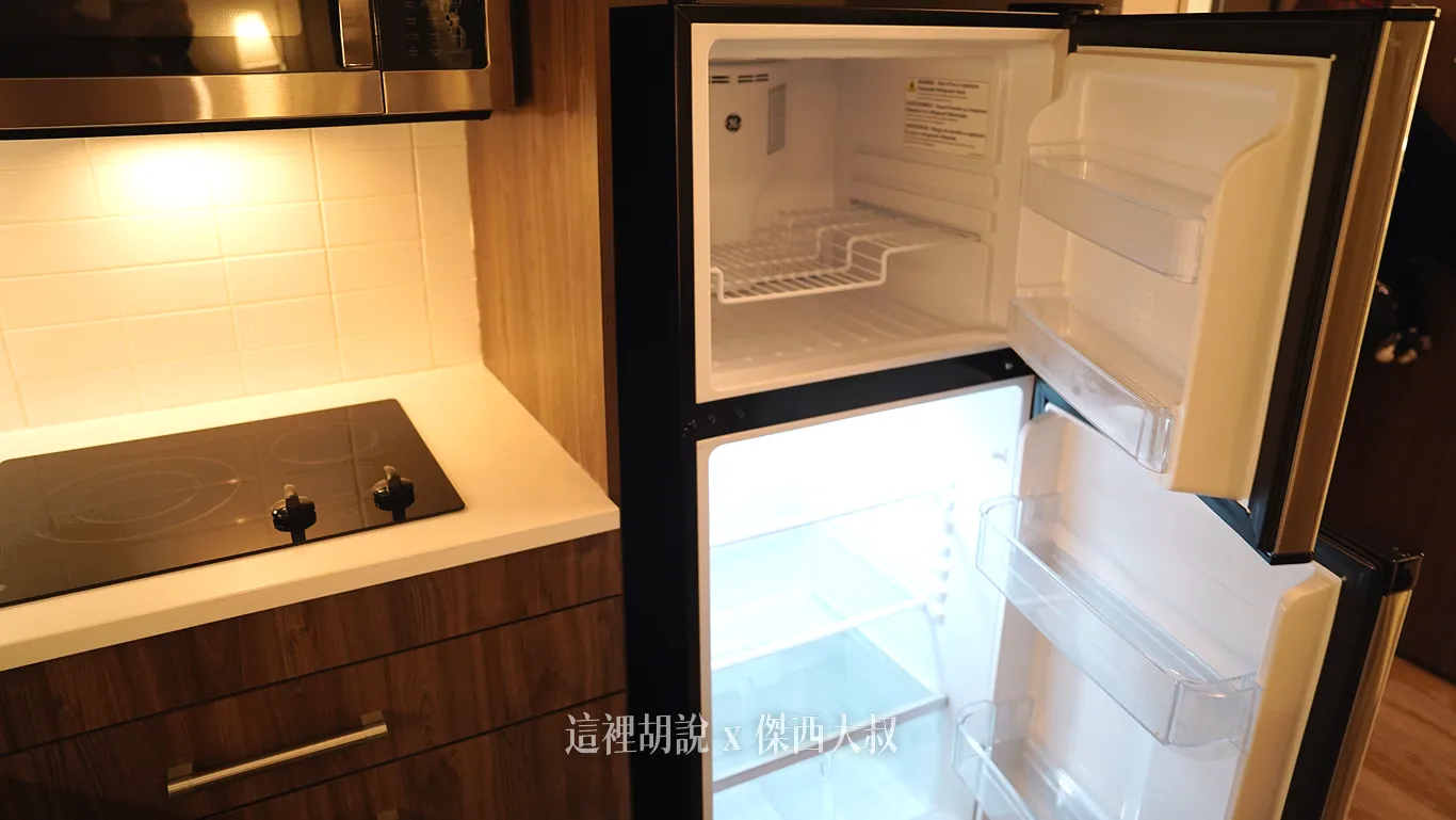 西雅圖機場Element Hotel廚房內配置全尺寸雙門冰箱，打開的上下層分別為冷凍與冷藏空間，內部層架乾淨明亮，左側緊鄰電磁爐與流理台，方便存放大量食材。