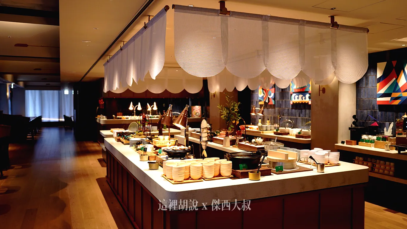 中央大中島自助餐檯上方掛著白色半透明布簾，檯面上整齊擺放著飯碗、日式木蓋鍋具與各式熱食主食，在暖色燈光下營造出舒適的用餐氛圍。