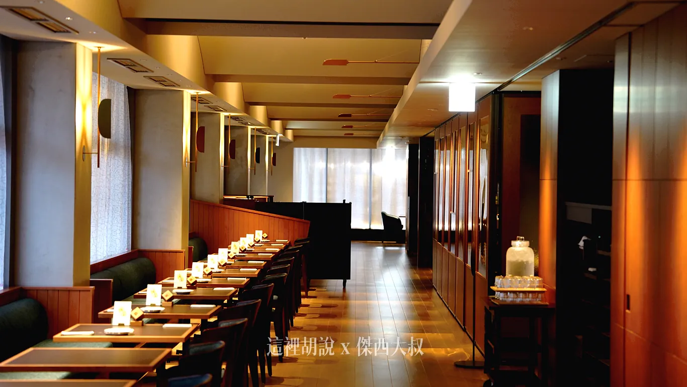 OMO DINING 採用溫暖木質調與柔和黃光設計，走道左側整齊排列著深色沙發與餐桌椅，沿著延伸的長廊走到底端右轉，還設有另一處寬敞的用餐空間。