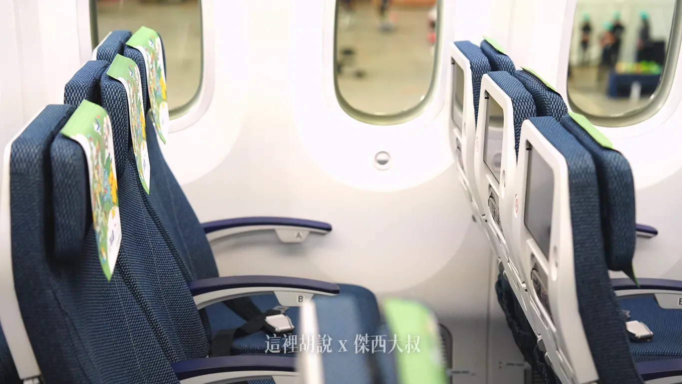 全日空波音787-9客艙經濟艙靠窗座位，深藍色織布座椅配備可調式頭枕與彩色頭墊巾，扶手採用輕薄型設計（遙控器移動到椅背），前方椅背設有個人娛樂螢幕。