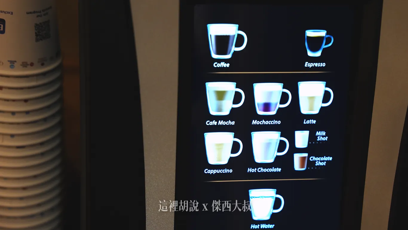 飯店早餐餐廳的自動咖啡機觸控螢幕上,以清晰圖示列出黑咖啡、義式濃縮、摩卡、拿鐵與熱巧克力等多種飲品選項,左側則整齊疊放著供房客外帶使用的紙杯。 飯店早餐餐廳的自動咖啡機觸控螢幕上,以清晰圖示列出黑咖啡、義式濃縮、摩卡、拿鐵與熱巧克力等多種飲品選項,左側則整齊疊放著供房客外帶使用的紙杯。