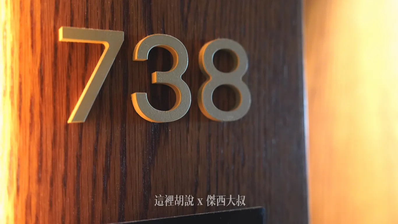 奧克蘭機場鉑爾曼飯店客房走廊上的房號標示，深色木質紋理門柱上鑲嵌立體金色數字，左側透出溫暖燈光勾勒出邊框細節。