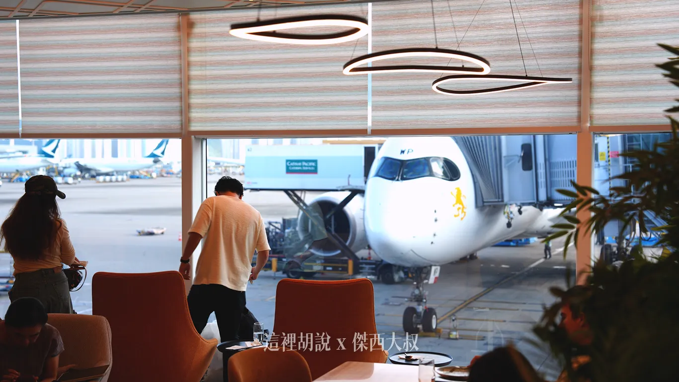 旅客坐在橘色高背扶手椅上,能一邊享用餐點一邊清楚眺望停機坪作業與遠處停放的航機。 旅客坐在橘色高背扶手椅上,能一邊享用餐點一邊清楚眺望停機坪作業與遠處停放的航機。