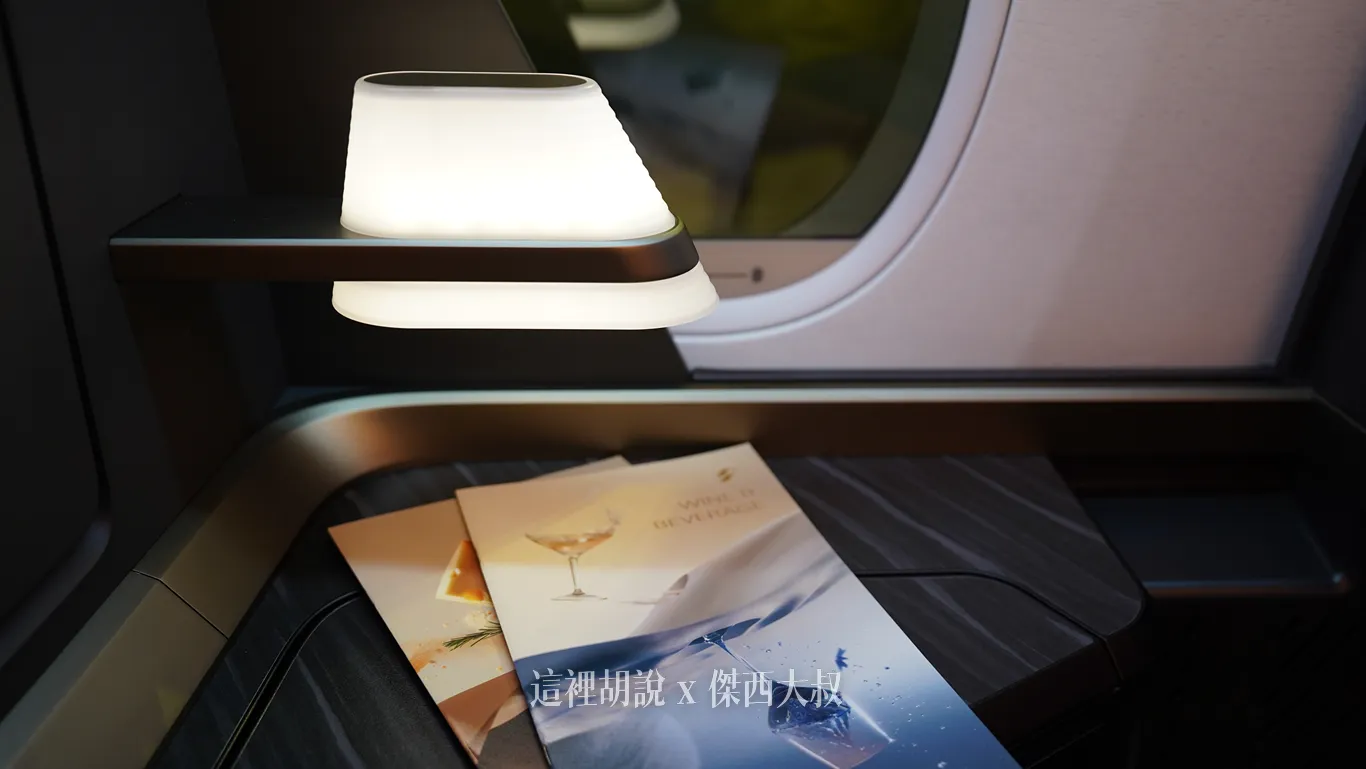 星宇航空商務艙座位旁設有一盞造型簡約且散發柔和白光的閱讀燈，側邊深色木紋置物平台上整齊擺放著供乘客入座時翻閱的酒單與精美餐單。