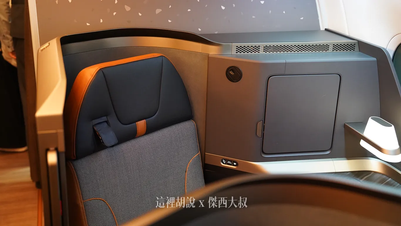 星宇航空商務艙座椅採用深灰色織布搭配皮革頭枕，邊緣以亮橘色皮革飾線滾邊跳色點綴，側邊包廂結構則設有閱讀燈、置物櫃與情境照明燈具。