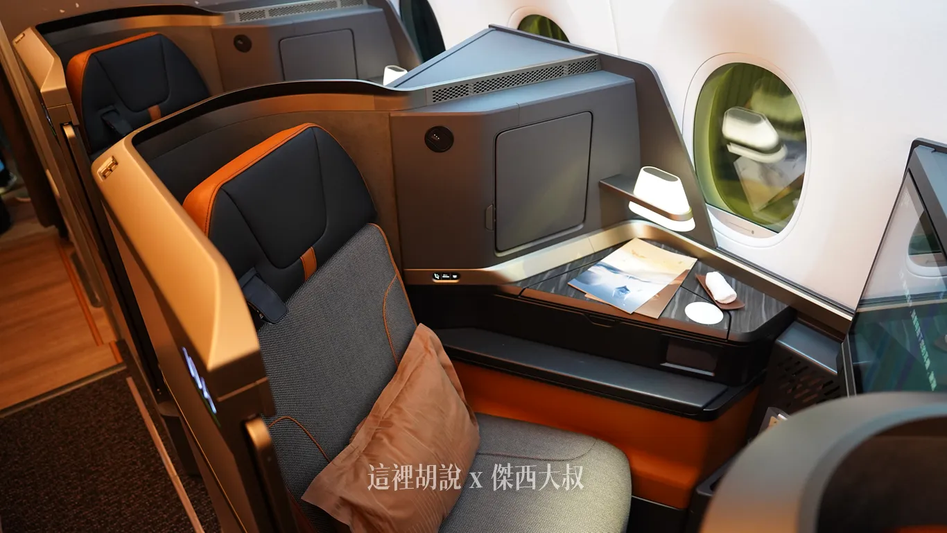 星宇航空商務艙客艙採反魚骨配置，灰色織布座椅搭配橘黑頭枕與靠枕，側邊延伸出木紋檯面、柔和情境閱讀燈與前方座位交錯形成的充裕腳部空間。